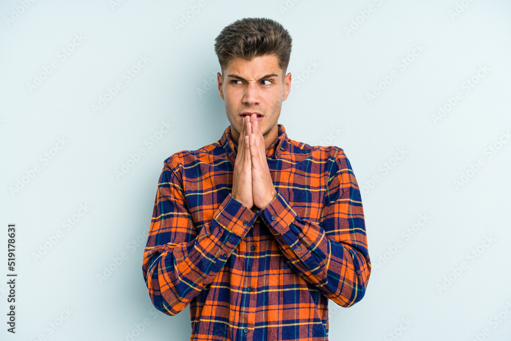 Young caucasian man isolated on blue background praying, showing devotion, religious person looking for divine inspiration. Young caucasian man isolated on blue background praying, showing devotion, religious person looking for divine inspiration.