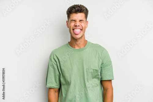 Young caucasian man isolated on white background funny and friendly sticking out tongue. © Asier