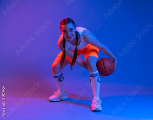 girl with a basketball in orange shorts, a t-shirt. an athlete in golfs and sneakers on a blue background plays the ball. Physical education teacher. basketball player. in move. blur. the game