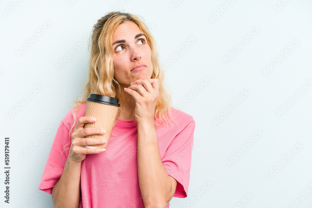 Young caucasian woman holding a take away coffee isolated on blue background looking sideways with doubtful and skeptical expression. Young caucasian woman holding a take away coffee isolated on blue background looking sideways with doubtful and skeptical expression.