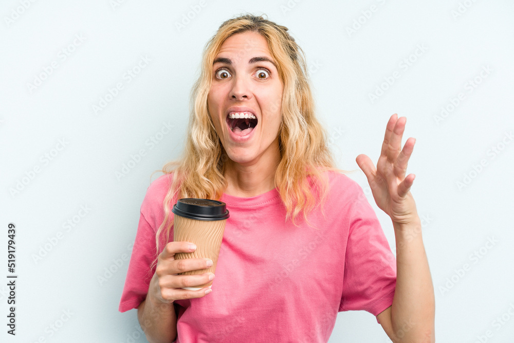 Young caucasian woman holding a take away coffee isolated on blue background receiving a pleasant surprise, excited and raising hands. Young caucasian woman holding a take away coffee isolated on blue background receiving a pleasant surprise, excited and raising hands.