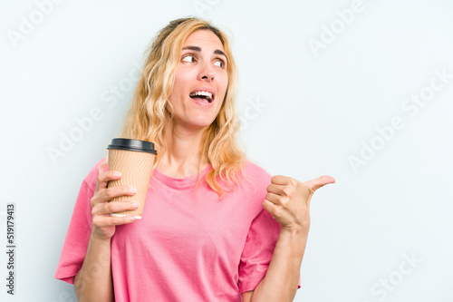 Young caucasian woman holding a take away coffee isolated on blue background points with thumb finger away, laughing and carefree.