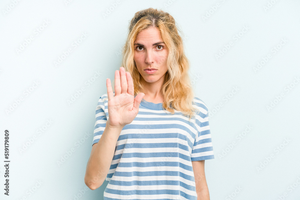 Young caucasian woman isolated on blue background standing with outstretched hand showing stop sign, preventing you.