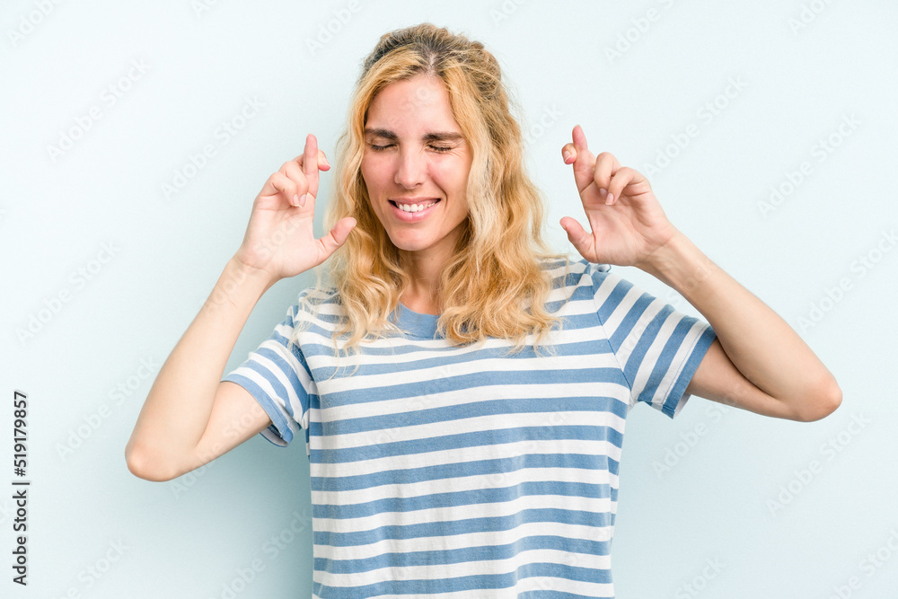 Young caucasian woman isolated on blue background crossing fingers for having luck Young caucasian woman isolated on blue background crossing fingers for having luck