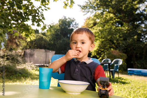 a cute little boy of three years is eating cornflakes outside