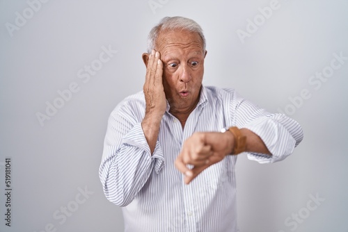 Senior man with grey hair standing over isolated background looking at the watch time worried, afraid of getting late © Krakenimages.com
