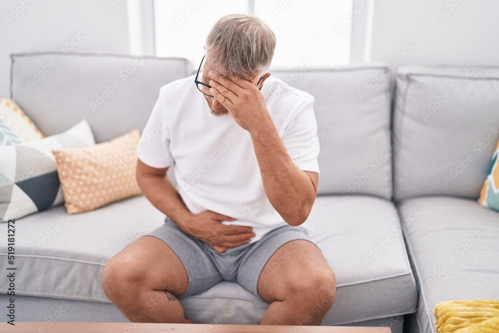 Middle age grey-haired man suffering for head and stomach ache at home Middle age grey-haired man suffering for head and stomach ache at home