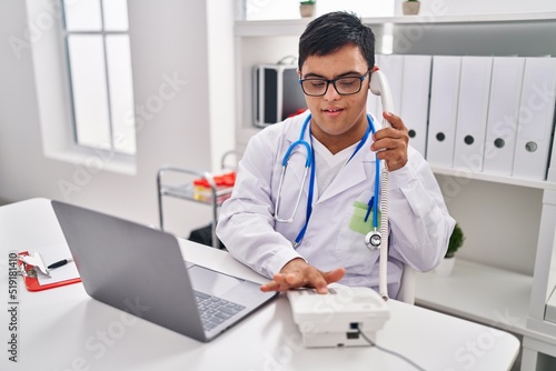 Down syndrome man wearing doctor uniform talking on the telephone at clinic