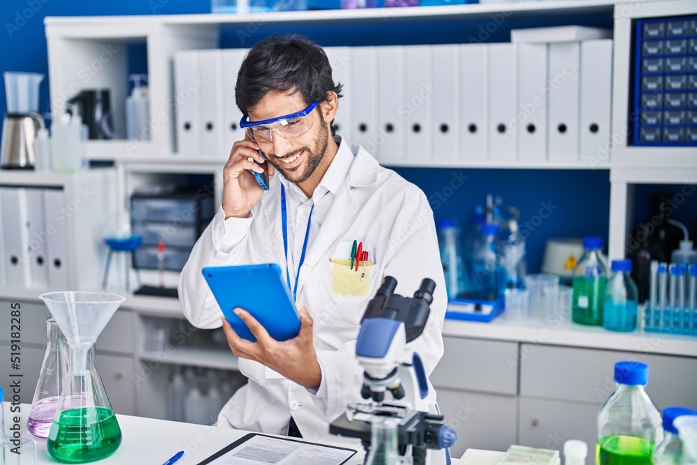 Young hispanic man scientist talking on the smartphone using touchpad at laboratory Young hispanic man scientist talking on the smartphone using touchpad at laboratory