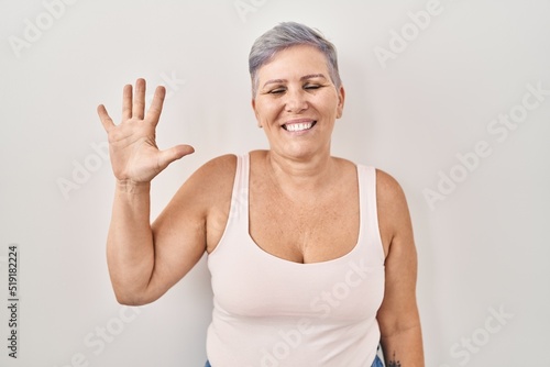 Middle age caucasian woman standing over white background showing and pointing up with fingers number five while smiling confident and happy.