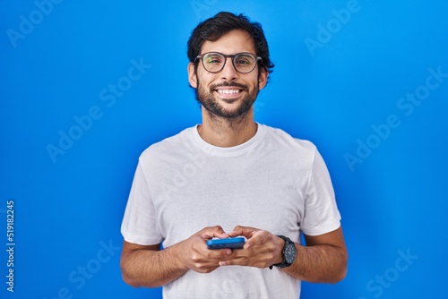 Handsome latin man using smartphone typing message smiling with a happy and cool smile on face. showing teeth.