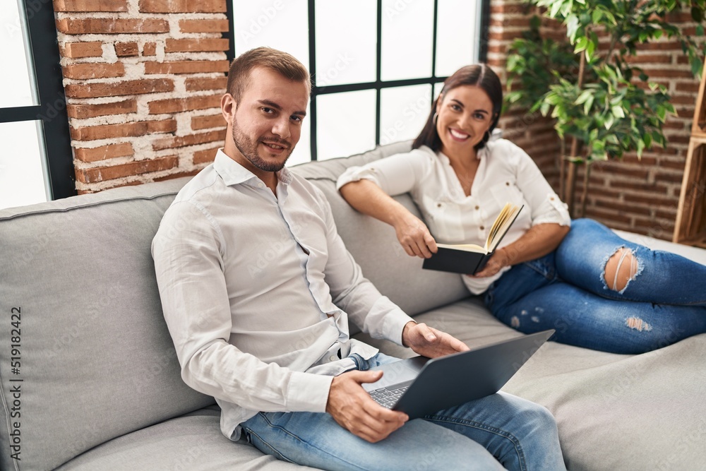 Obraz premium Man and woman couple using laptop and reading book at home