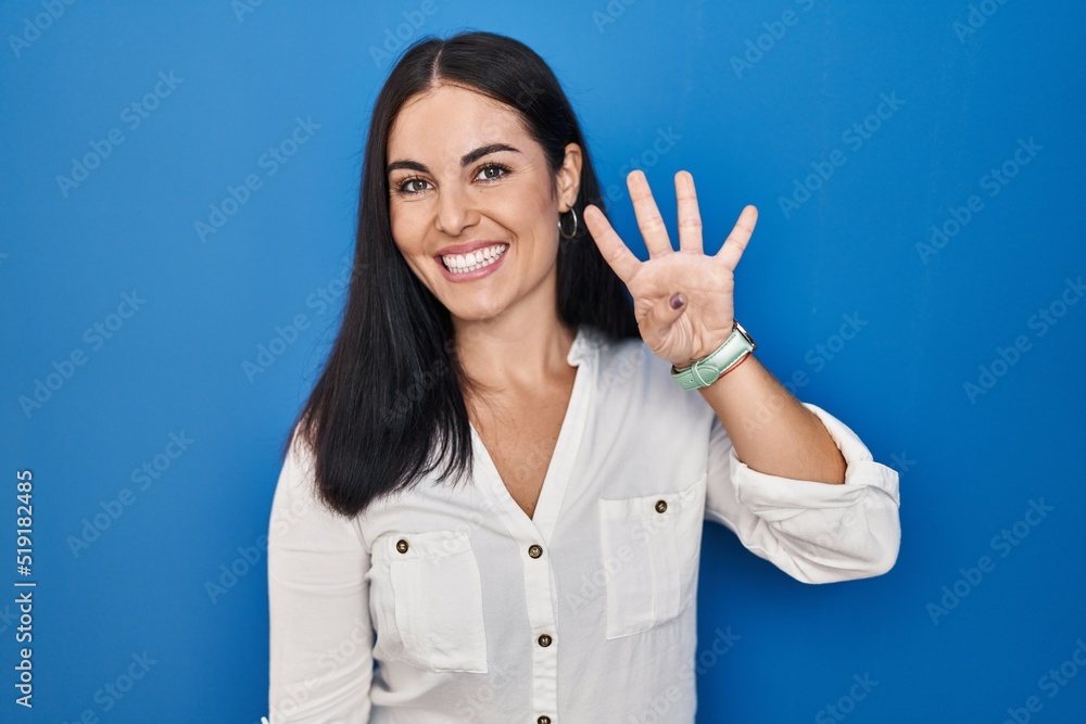Young hispanic woman standing over blue background showing and pointing up with fingers number four while smiling confident and happy. Young hispanic woman standing over blue background showing and pointing up with fingers number four while smiling confident and happy.
