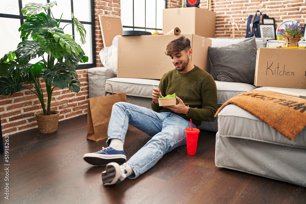 Young arab man eating take away salad sitting on floor at new home