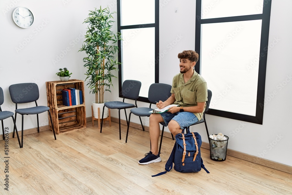 Young arab man writing on clipboard sitting on the chair at waiting room Young arab man writing on clipboard sitting on the chair at waiting room