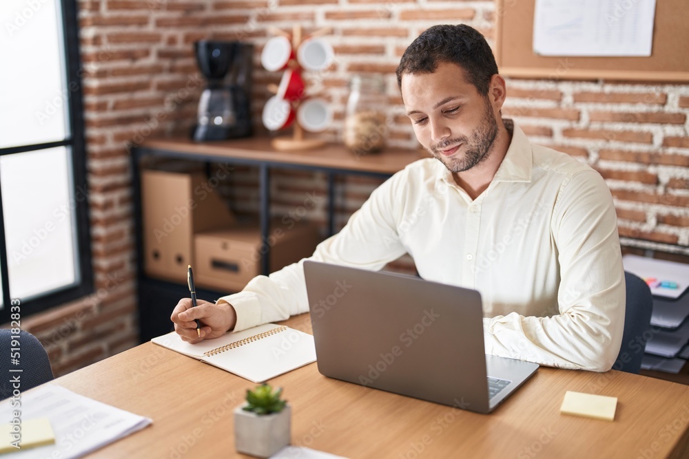 Young man business worker using laptop writing on notebook at office Young man business worker using laptop writing on notebook at office