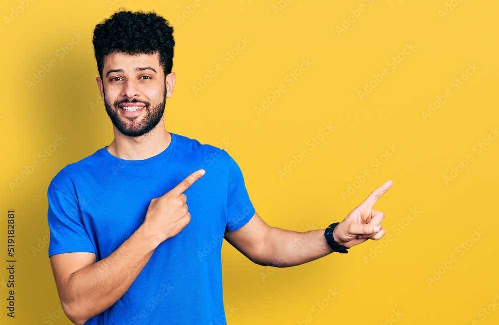 Young arab man with beard wearing casual blue t shirt smiling and looking at the camera pointing with two hands and fingers to the side. Young arab man with beard wearing casual blue t shirt smiling and looking at the camera pointing with two hands and fingers to the side.