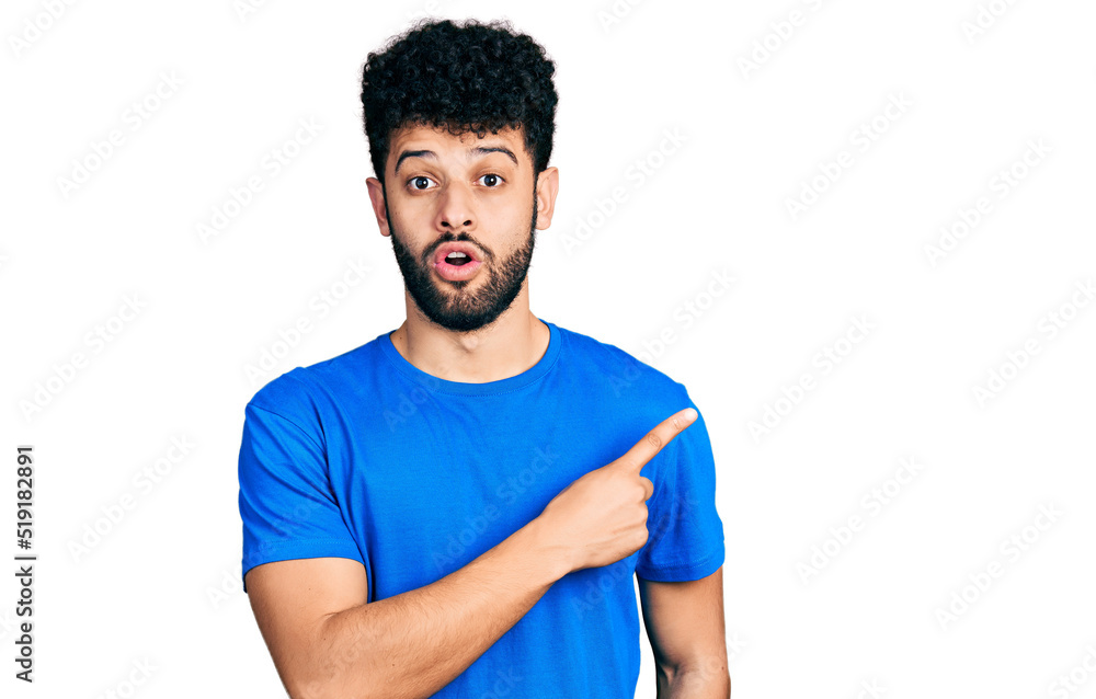 Young arab man with beard wearing casual blue t shirt surprised pointing with finger to the side, open mouth amazed expression. Young arab man with beard wearing casual blue t shirt surprised pointing with finger to the side, open mouth amazed expression.
