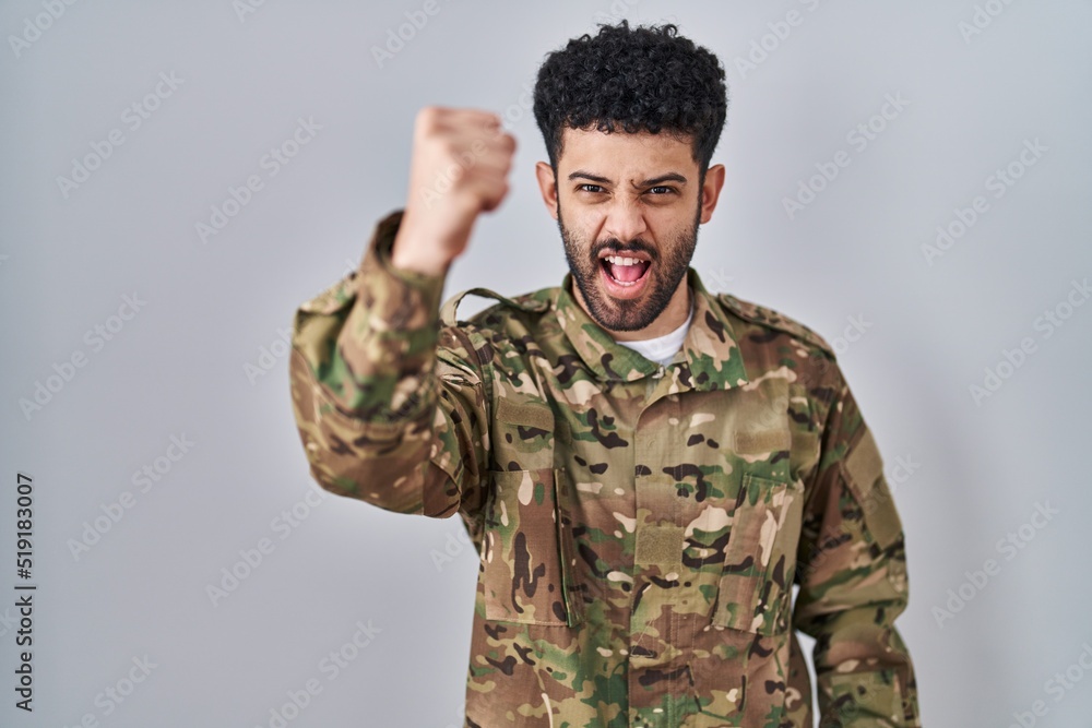 Arab man wearing camouflage army uniform angry and mad raising fist frustrated and furious while shouting with anger. rage and aggressive concept.