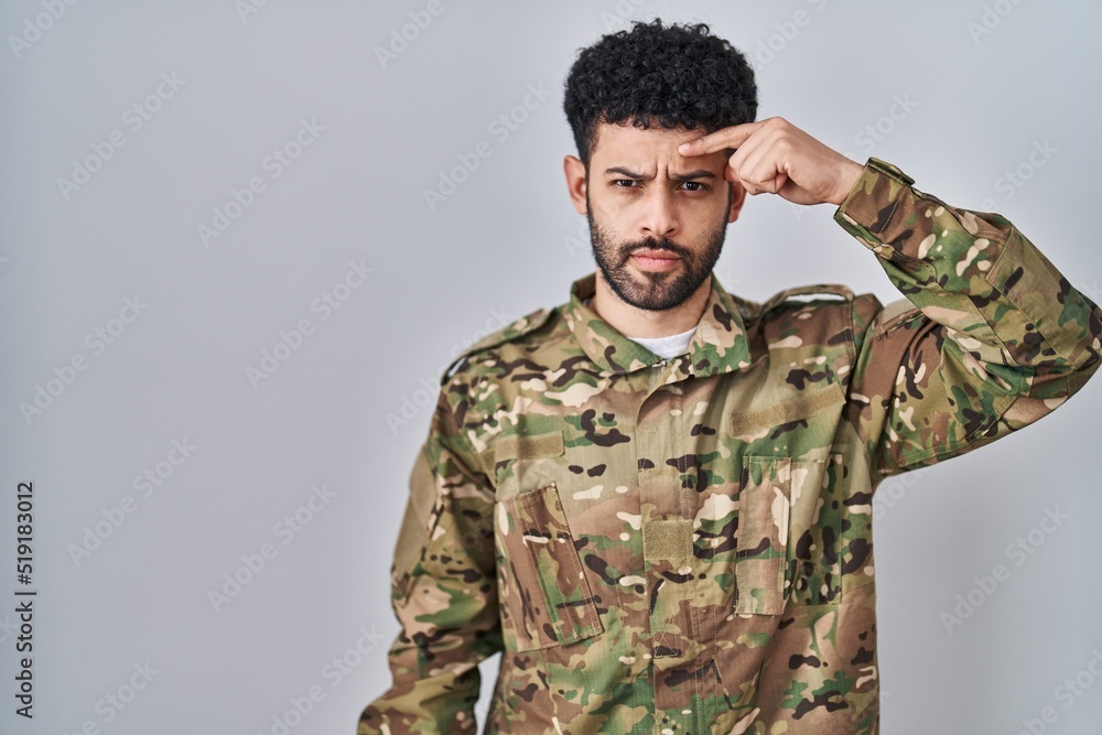Arab man wearing camouflage army uniform pointing unhappy to pimple on forehead, ugly infection of blackhead. acne and skin problem Arab man wearing camouflage army uniform pointing unhappy to pimple on forehead, ugly infection of blackhead. acne and skin problem