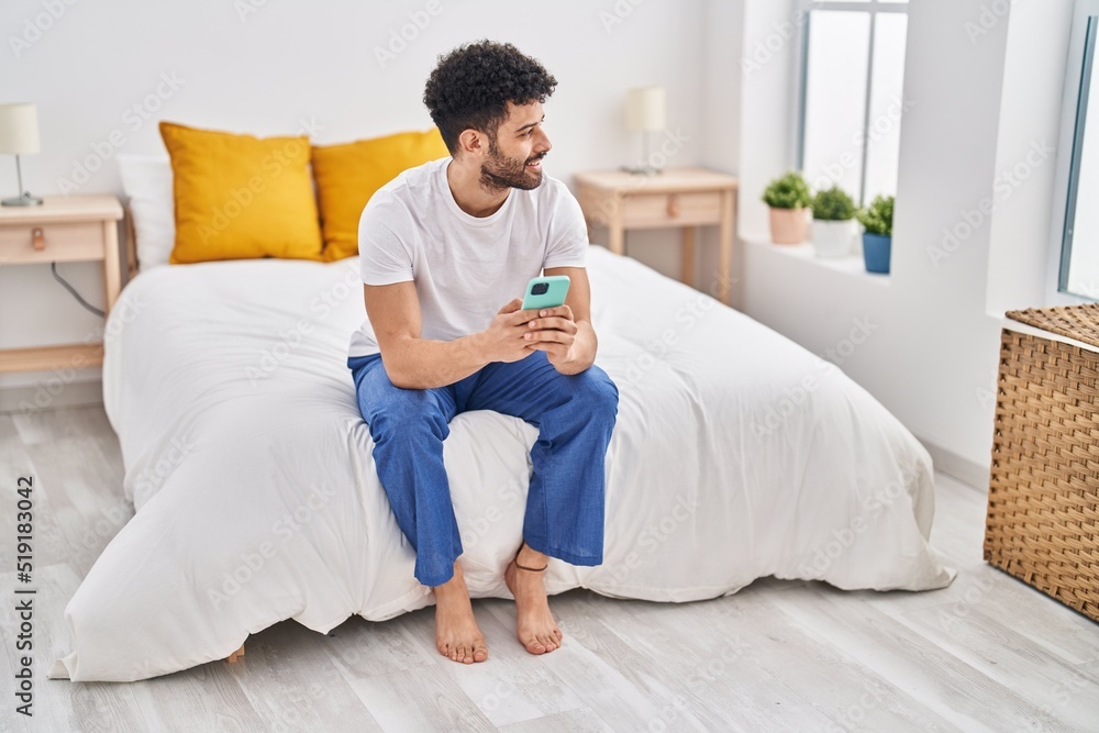 Young arab man using smartphone sitting on bed at bedroom Young arab man using smartphone sitting on bed at bedroom