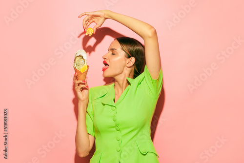 Young beautiful woman squeezing lemon on delicious oyster in ice cream cone isolated over pink background