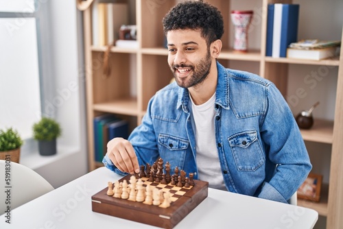 Young arab man playing chess sitting on table at home