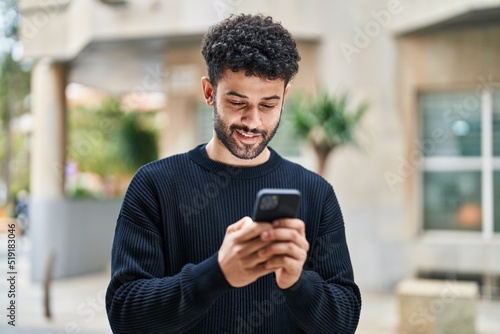 Young arab man smiling confident using smartphone at street
