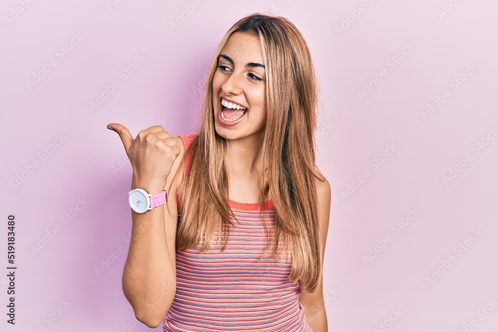 Beautiful hispanic woman wearing casual summer t shirt smiling with happy face looking and pointing to the side with thumb up. Beautiful hispanic woman wearing casual summer t shirt smiling with happy face looking and pointing to the side with thumb up.