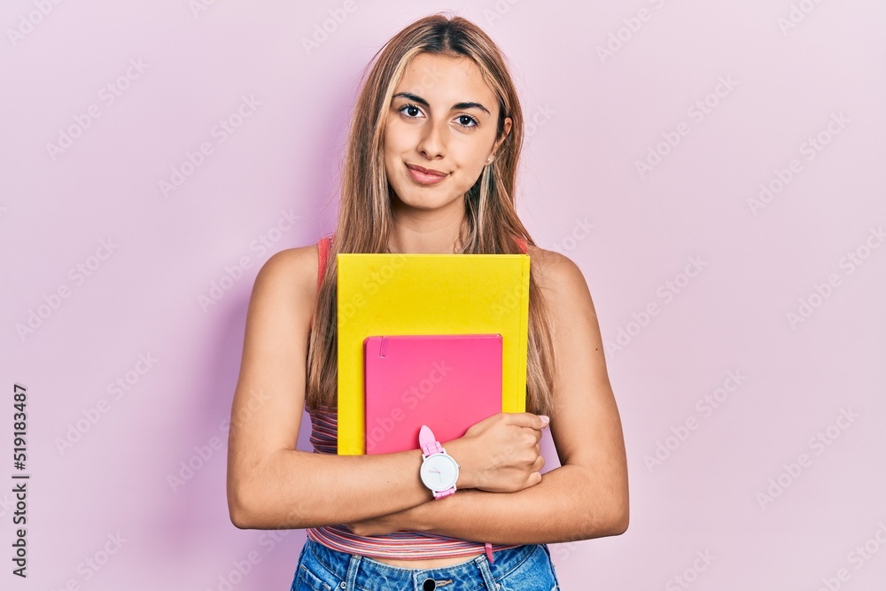 Beautiful hispanic woman holding books thinking attitude and sober expression looking self confident