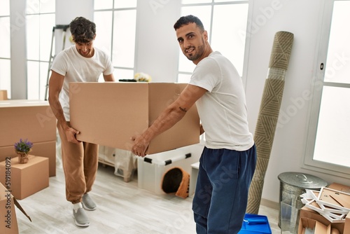 Two hispanic men couple smiling confident holding cardboard box at new home