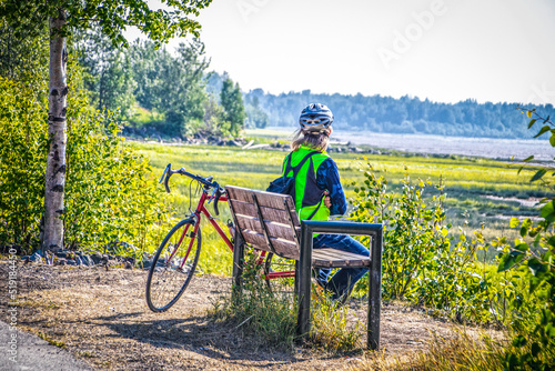 Canvas Print Long haired person in blue jeans with backpack and helment sits looking out at b