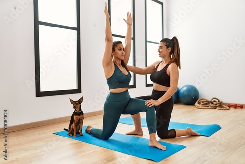 Two women smiling confident training yoga with dog at sport center