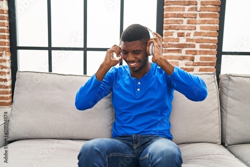 Young african american man listening to music sitting on sofa at home