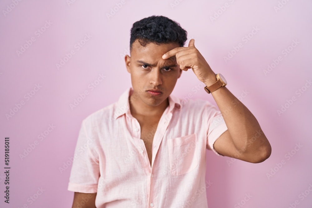 Young hispanic man standing over pink background pointing unhappy to pimple on forehead, ugly infection of blackhead. acne and skin problem Young hispanic man standing over pink background pointing unhappy to pimple on forehead, ugly infection of blackhead. acne and skin problem
