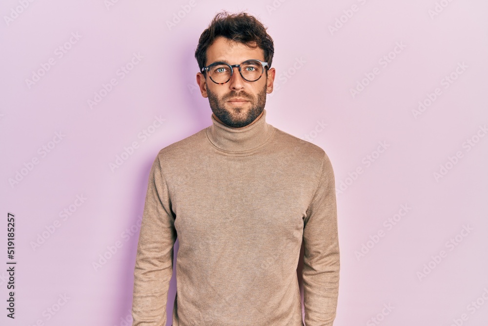 Fototapeta premium Handsome man with beard wearing turtleneck sweater and glasses relaxed with serious expression on face. simple and natural looking at the camera.