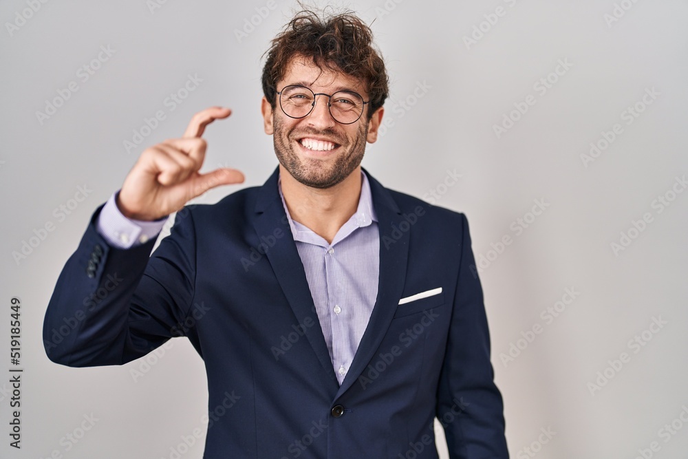 Hispanic business man wearing glasses smiling and confident gesturing with hand doing small size sign with fingers looking and the camera. measure concept. Hispanic business man wearing glasses smiling and confident gesturing with hand doing small size sign with fingers looking and the camera. measure concept.
