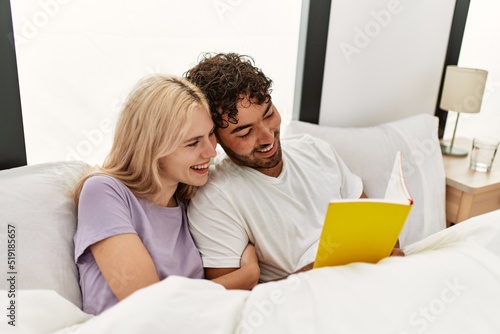 Young beautiful couple reading book lying in bed at home.