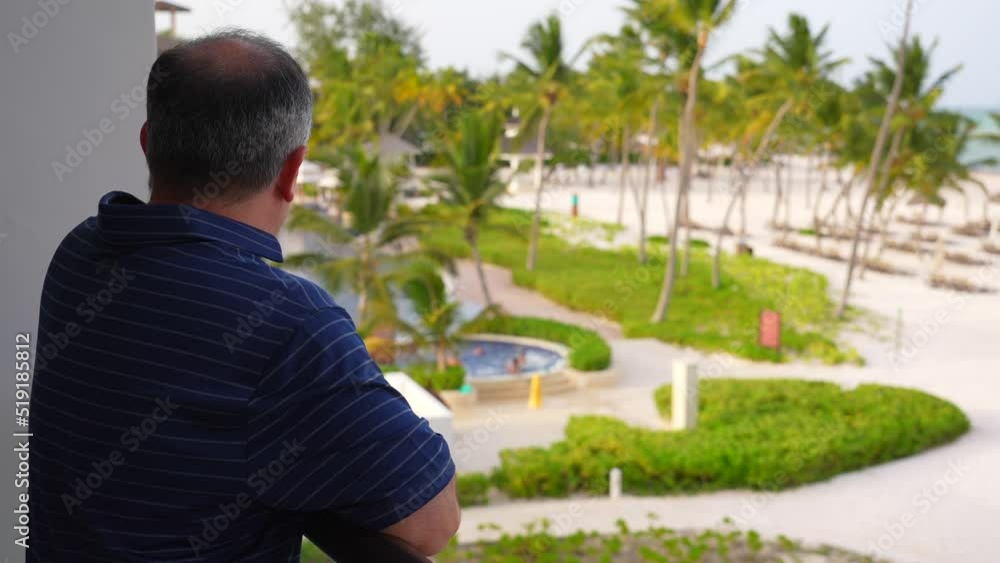 Man looking at resort property from balcony. Palm trees, beach and pool scenery. Vacation theme. Man looking at resort property from balcony. Palm trees, beach and pool scenery. Vacation theme.