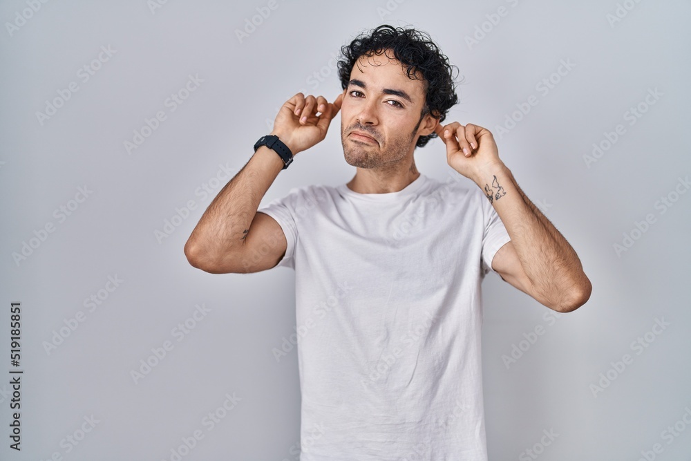 Hispanic man standing over isolated background smiling pulling ears with fingers, funny gesture. audition problem Hispanic man standing over isolated background smiling pulling ears with fingers, funny gesture. audition problem