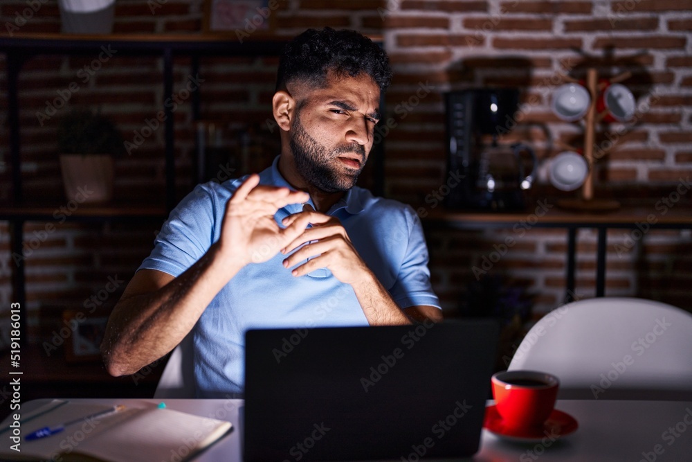 Hispanic man with beard using laptop at night disgusted expression, displeased and fearful doing disgust face because aversion reaction. with hands raised Hispanic man with beard using laptop at night disgusted expression, displeased and fearful doing disgust face because aversion reaction. with hands raised