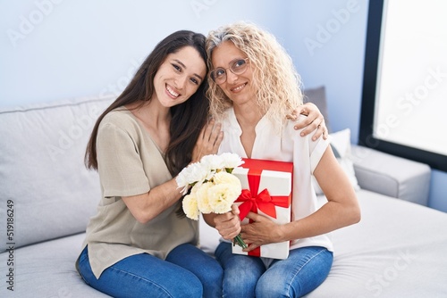 Two women mother and daughter surprise with gift and flowers at home