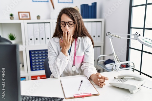 Young doctor woman wearing doctor uniform and stethoscope at the clinic bored yawning tired covering mouth with hand. restless and sleepiness.