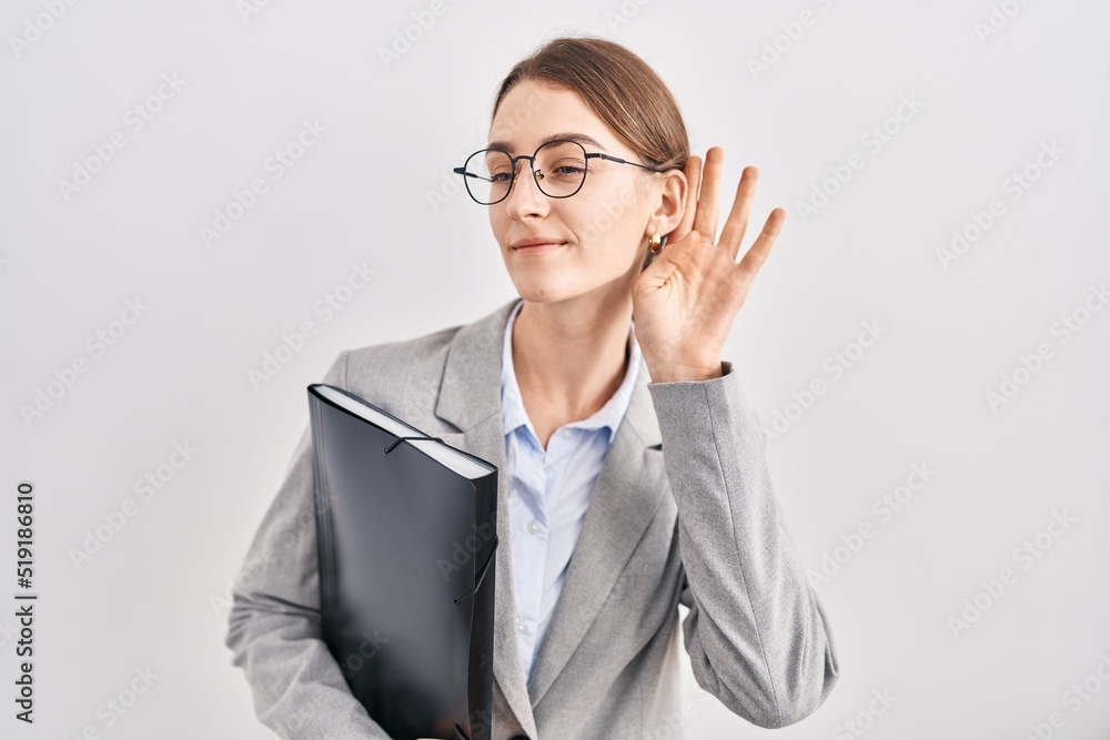 Young caucasian woman wearing business clothes and glasses smiling with hand over ear listening an hearing to rumor or gossip. deafness concept. Young caucasian woman wearing business clothes and glasses smiling with hand over ear listening an hearing to rumor or gossip. deafness concept.