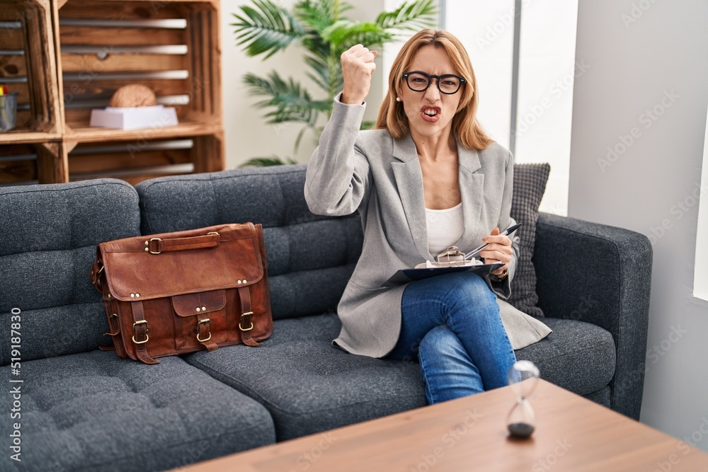 Hispanic woman working at consultation office angry and mad raising fist frustrated and furious while shouting with anger. rage and aggressive concept. Hispanic woman working at consultation office angry and mad raising fist frustrated and furious while shouting with anger. rage and aggressive concept.