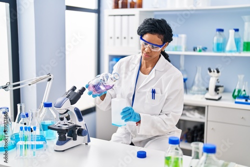 African american woman wearing scientist uniform measuring liquid at laboratory