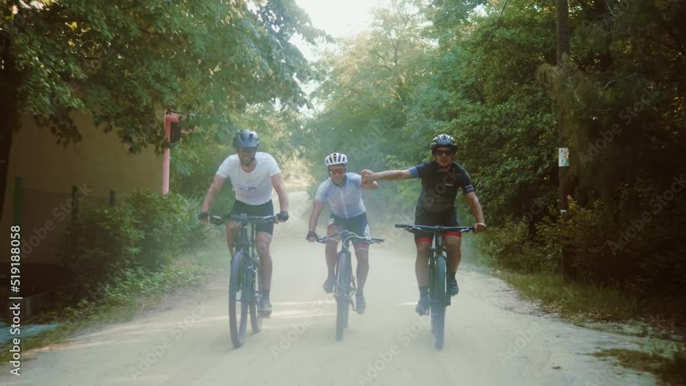 Young mtb bikers giving high fives while riding on a dirt road on the mountain Young mtb bikers giving high fives while riding on a dirt road on the mountain
