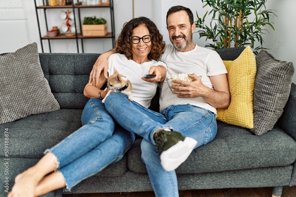 Middle age hispanic couple watching movie and eating popcorn sitting on the sofa at home. Middle age hispanic couple watching movie and eating popcorn sitting on the sofa at home.