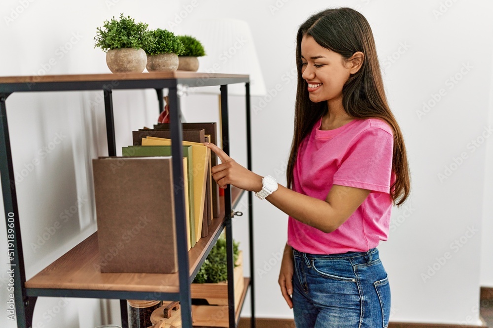 Young latin woman smiling confident choosing book of shelving at home Young latin woman smiling confident choosing book of shelving at home