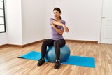 Young latin woman stretching using fit ball at sport center